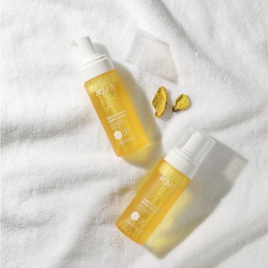 Dos botes del limpiador facial de cúrcuma de JEJUON sobre una toalla blanca, representando la línea de productos de la marca.